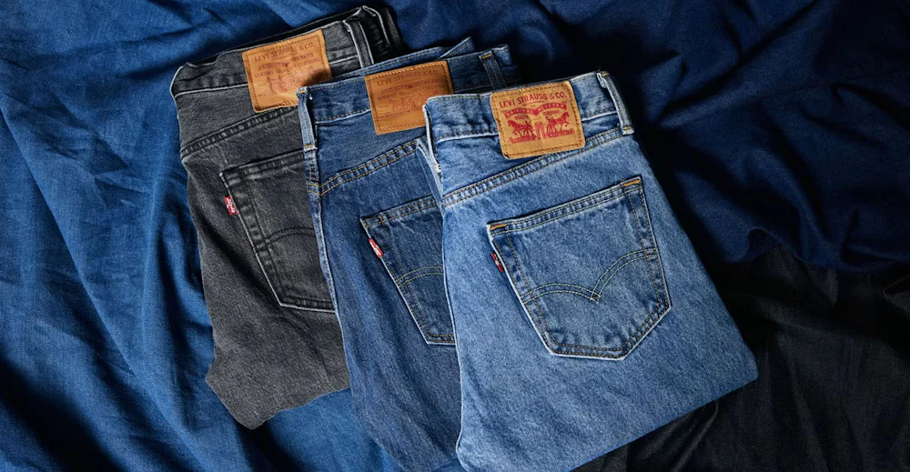 Kolme paria Levi Strauss & Co. -farkkuja eri väreissä: musta, tummansininen ja vaaleansininen, taiteltuina siniselle kankaalle.