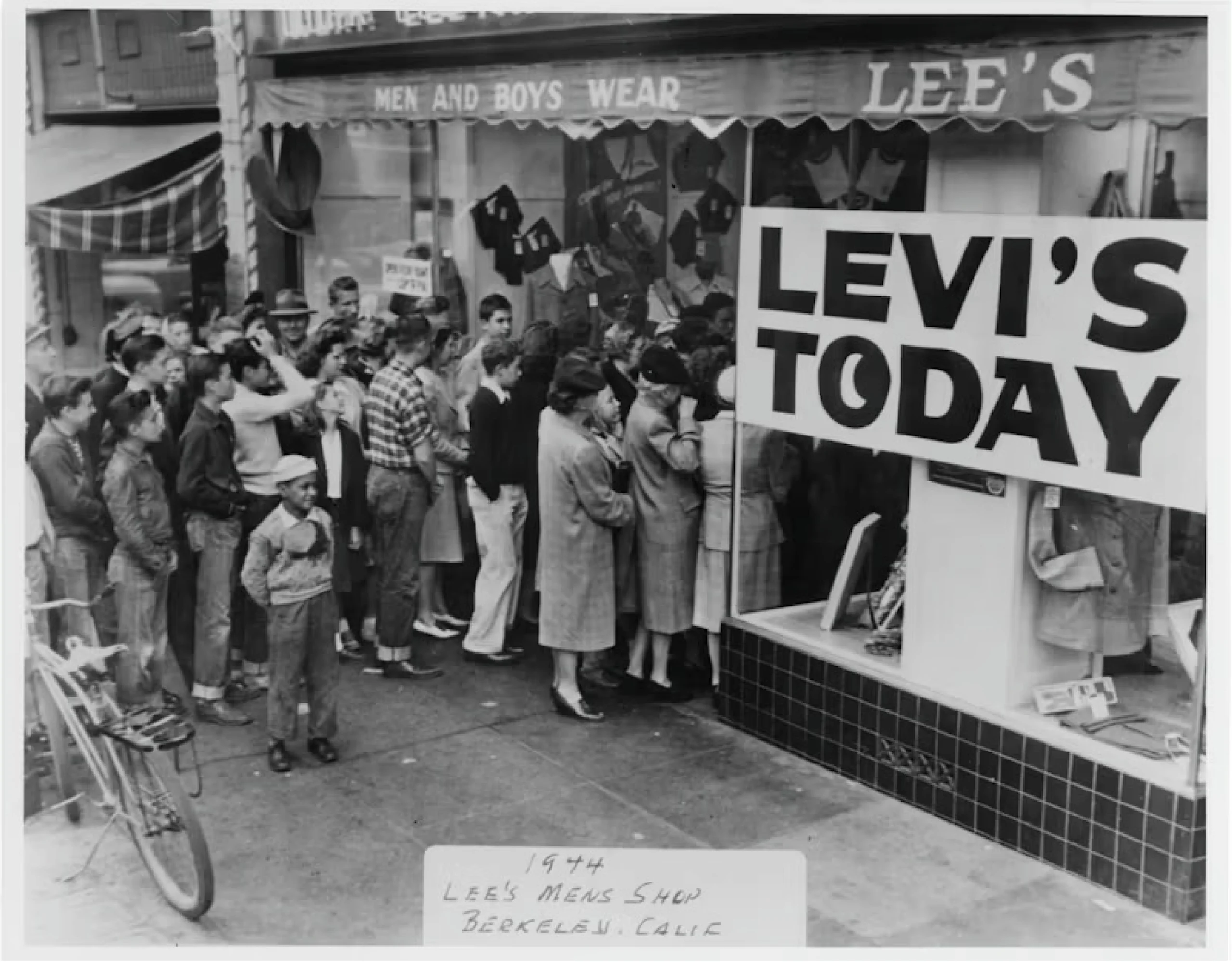 En grupp män, kvinnor och pojkar stod uppradade utanför ett butikfönster märkt "LEVI'S TODAY" och väntade på att få komma in i klädaffären.