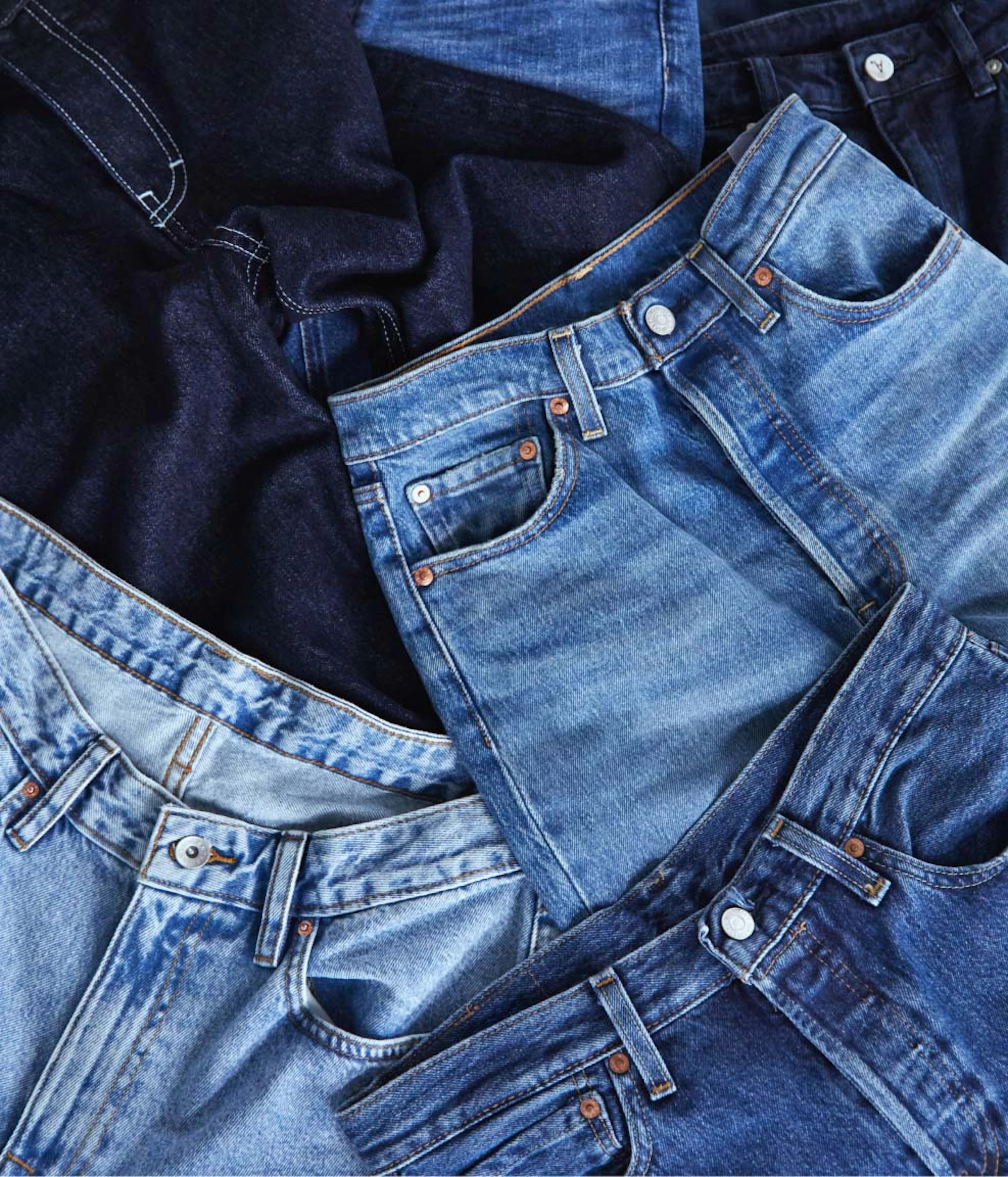 Flat lay of assorted denim jeans from brands including Levi’s, Lee, Replay, True Religion, and Va Vite, arranged in a piled stack and photographed from above.