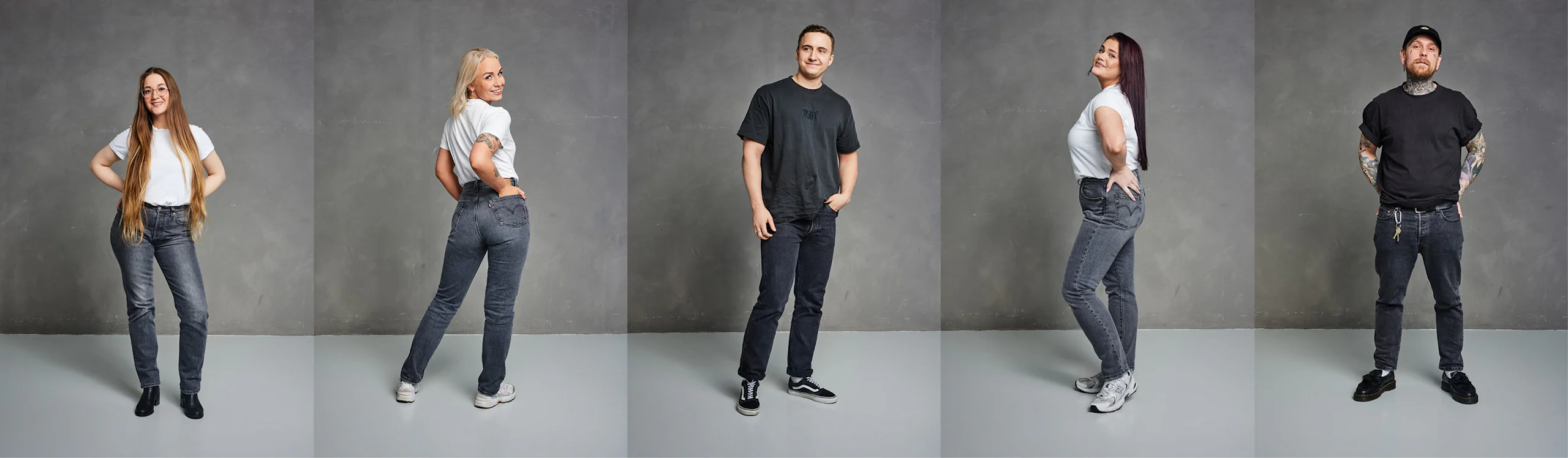 Fem vuxna i olika åldrar som bär vita eller svarta t-shirts och grå jeans, poserar självsäkert mot en neutral studiobakgrund.