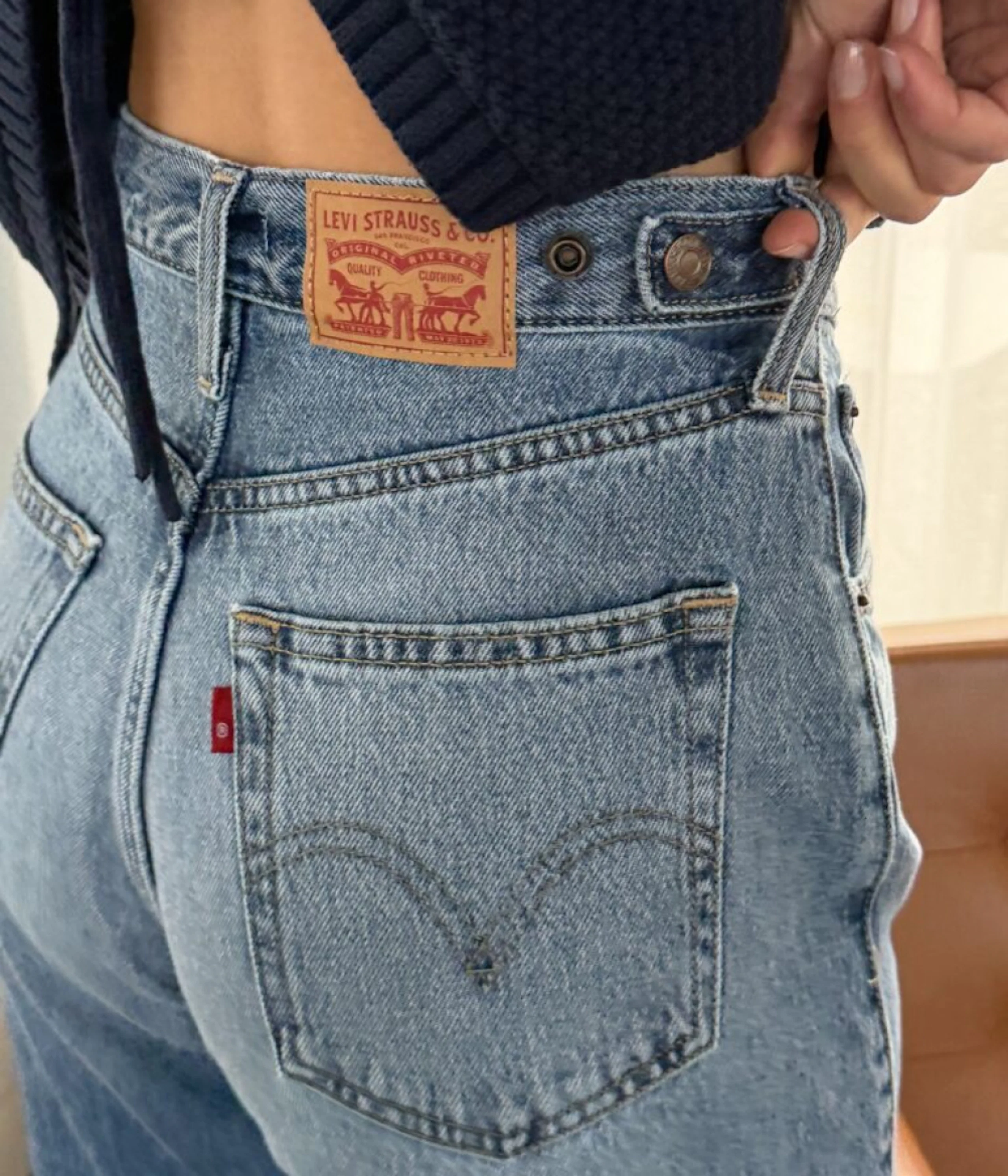 Nærbilde av lyseblå Levi Strauss & Co. jeans med ikonisk lærmerke og baklomme, kombinert med mørk strikket topp.