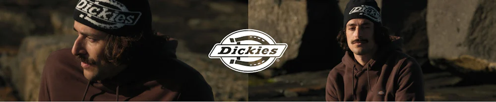 Mies yllään ruskea Dickies-huppari ja Dickies-pipo ulkona kivien edessä. Dickies-logo keskellä.