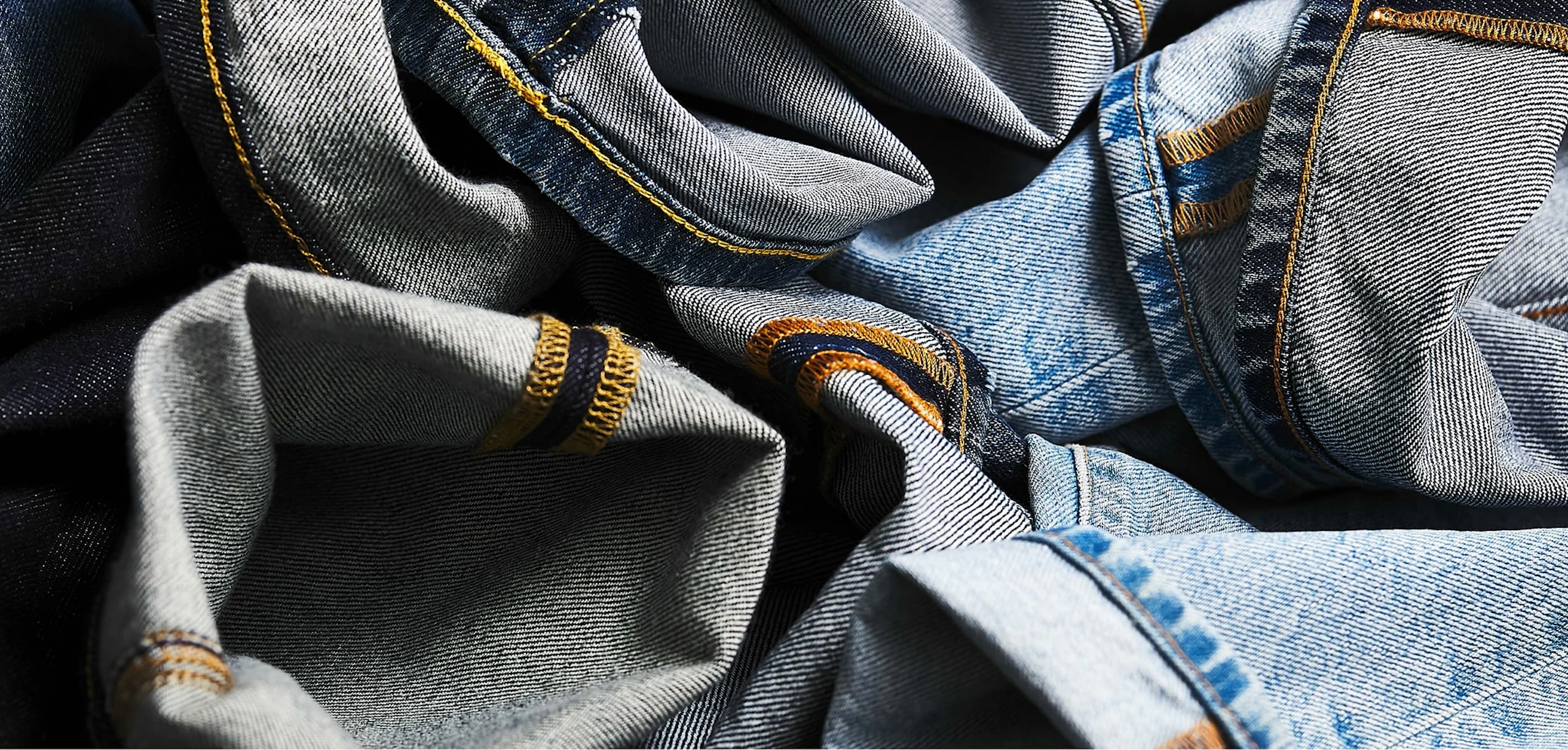 Närbild av skrynkliga blå denimjeans som visar uppvikta fållar, orange topplist och synlig twillstruktur.