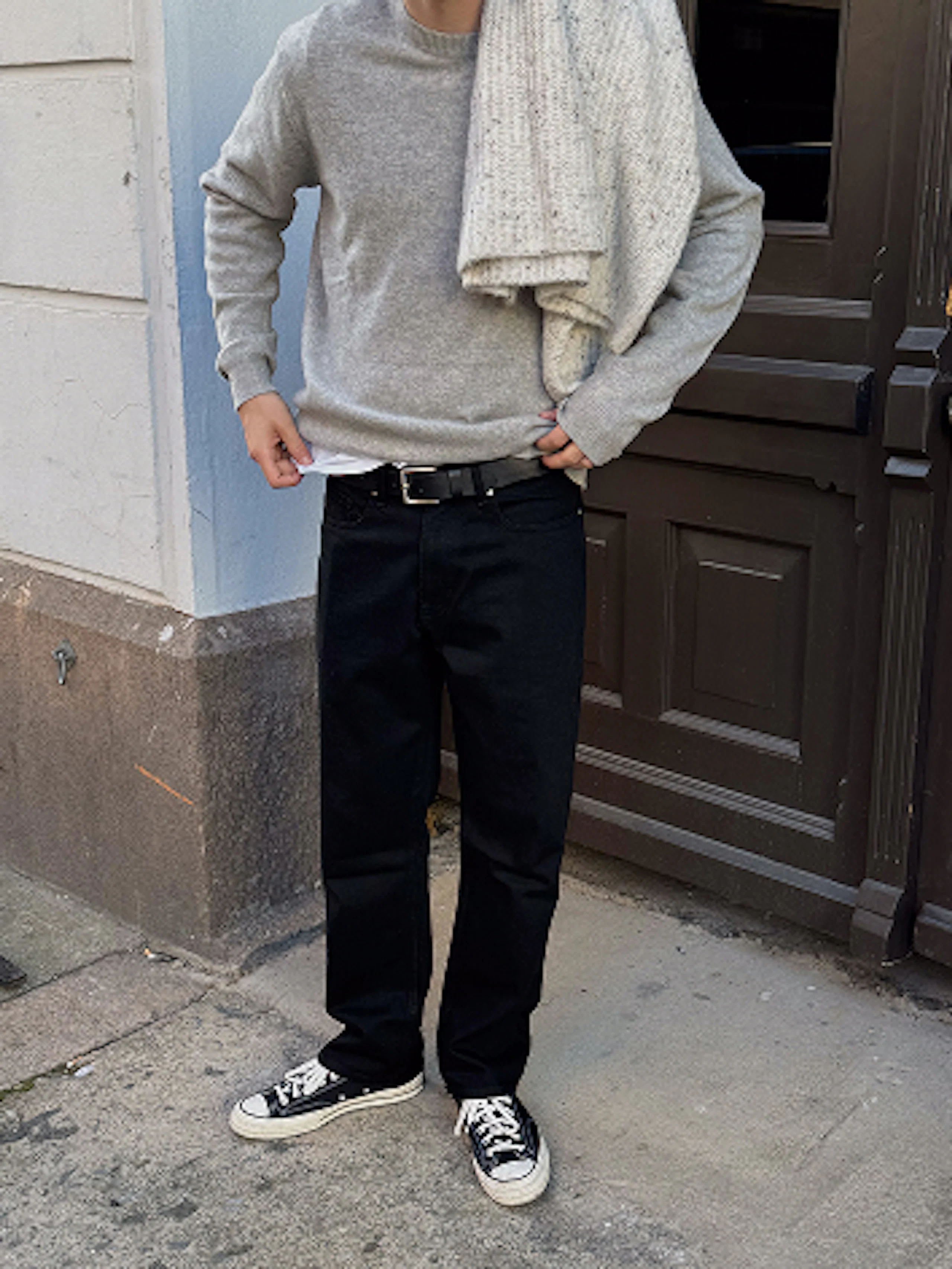 Person i grå genser, svarte bukser og svarte Converse-sko, med et beige skjerf over skulderen.
