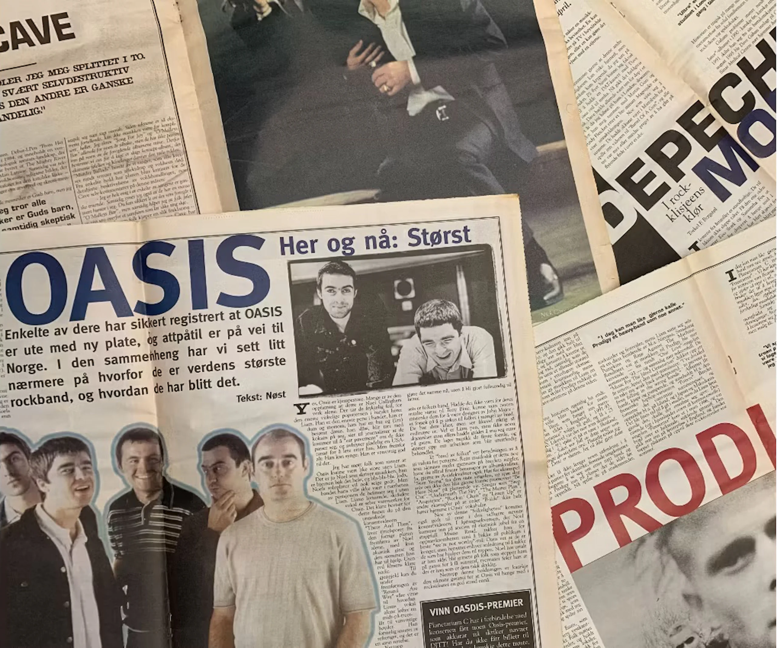 Tidningsuppslag med en stor "OASIS"-rubrik, bandbilder och artiklar om britpopgrupper upplagda på ett bord.