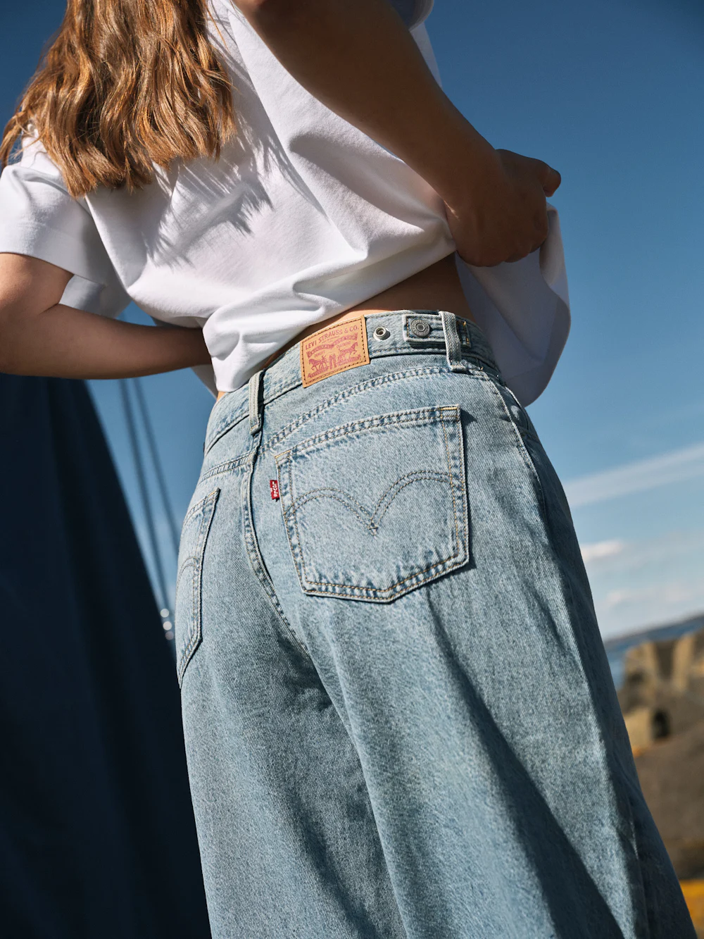 Nainen yllään vaaleat Levi's-farkut ja valkoinen t-paita. Lähikuva farkkujen takaosasta, sininen taivas taustalla.