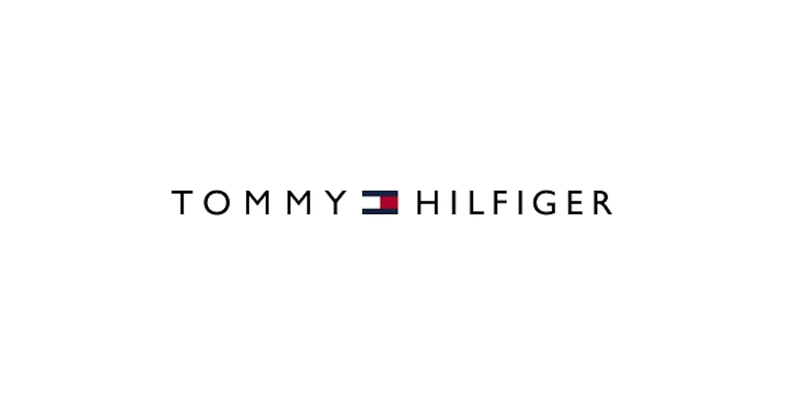 Tommy Hilfiger -logo valkoisella taustalla, teksti mustalla ja pieni punainen, valkoinen ja sininen lippukuvake keskellä.
