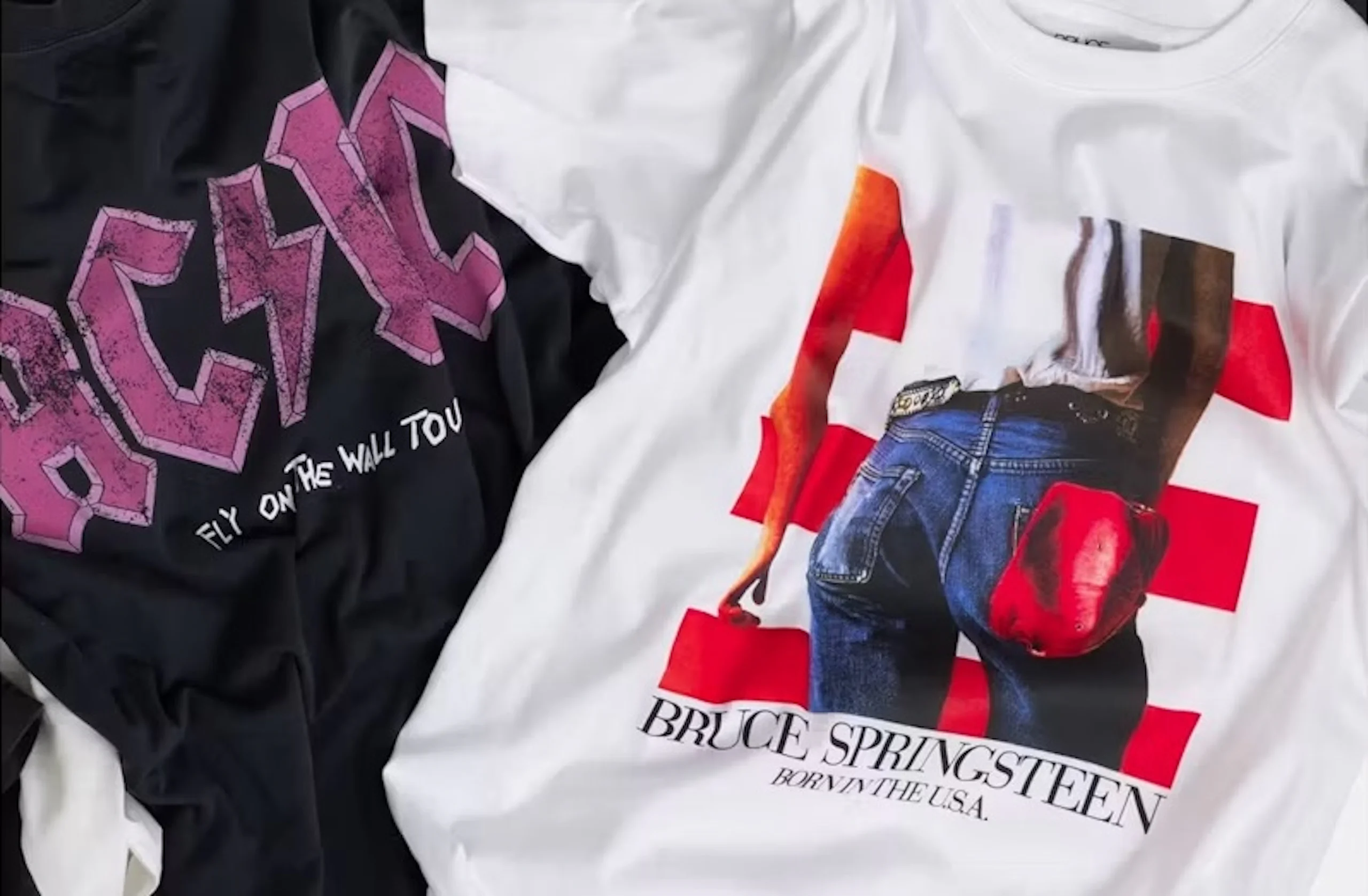 Kaksi taiteltua rock-bändipaitaa: musta AC/DC-paita pinkillä logolla ja "Fly on the Wall Tour" -tekstillä sekä valkoinen Bruce Springsteenin "Born in the U.S.A." -paita, jossa farkkuja ja punaista lakkia pitelevä henkilö.