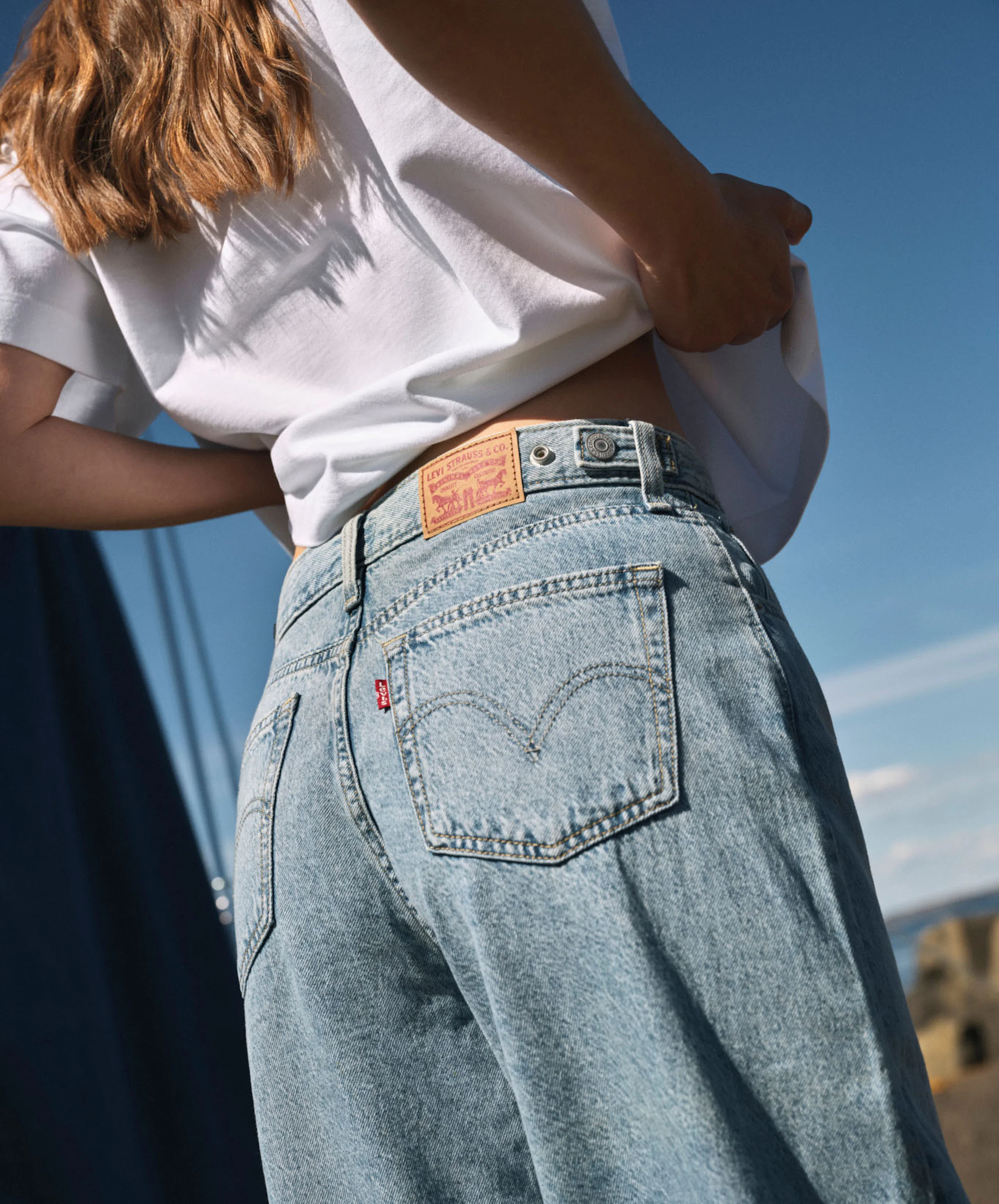 Närbild bakifrån på person i ljusblå Levi's jeans och vit t-shirt mot blå himmel.