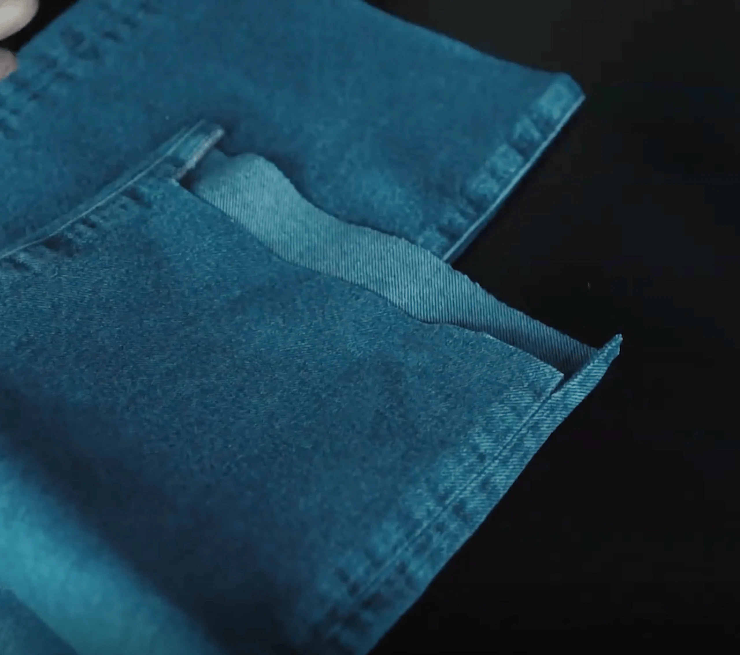 Nærbilde av sammenlagte lag av blå denimstoff og sømkanter lagt på en mørk overflate, som viser tekstur og stingdetaljer.
