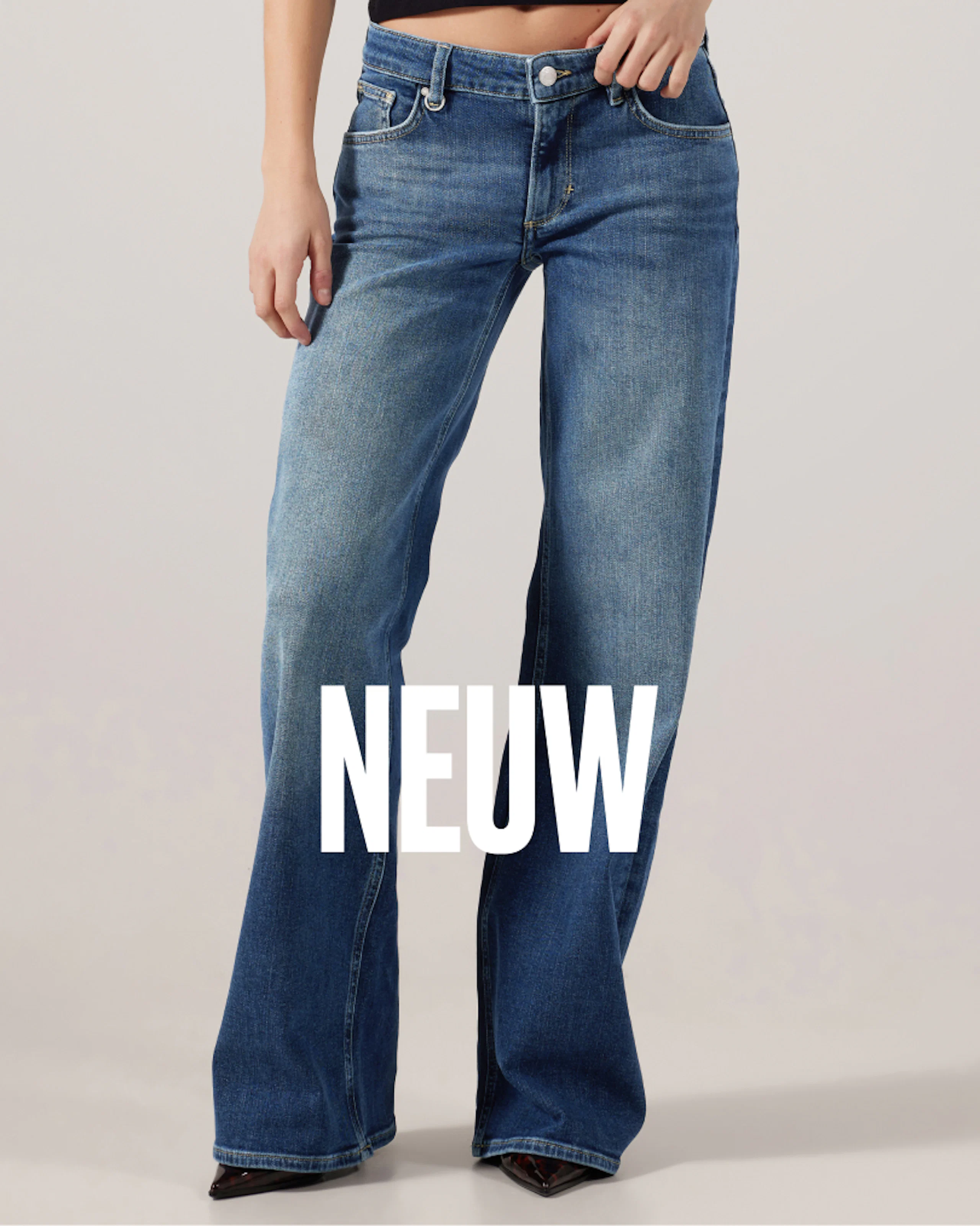 Kvinna som bär lågmidjade jeans i blå denim med vida ben och urtvättad tvätt, parat med mörka spetsiga klackar. NEUW:s varumärkeslogotyp överlagrad.