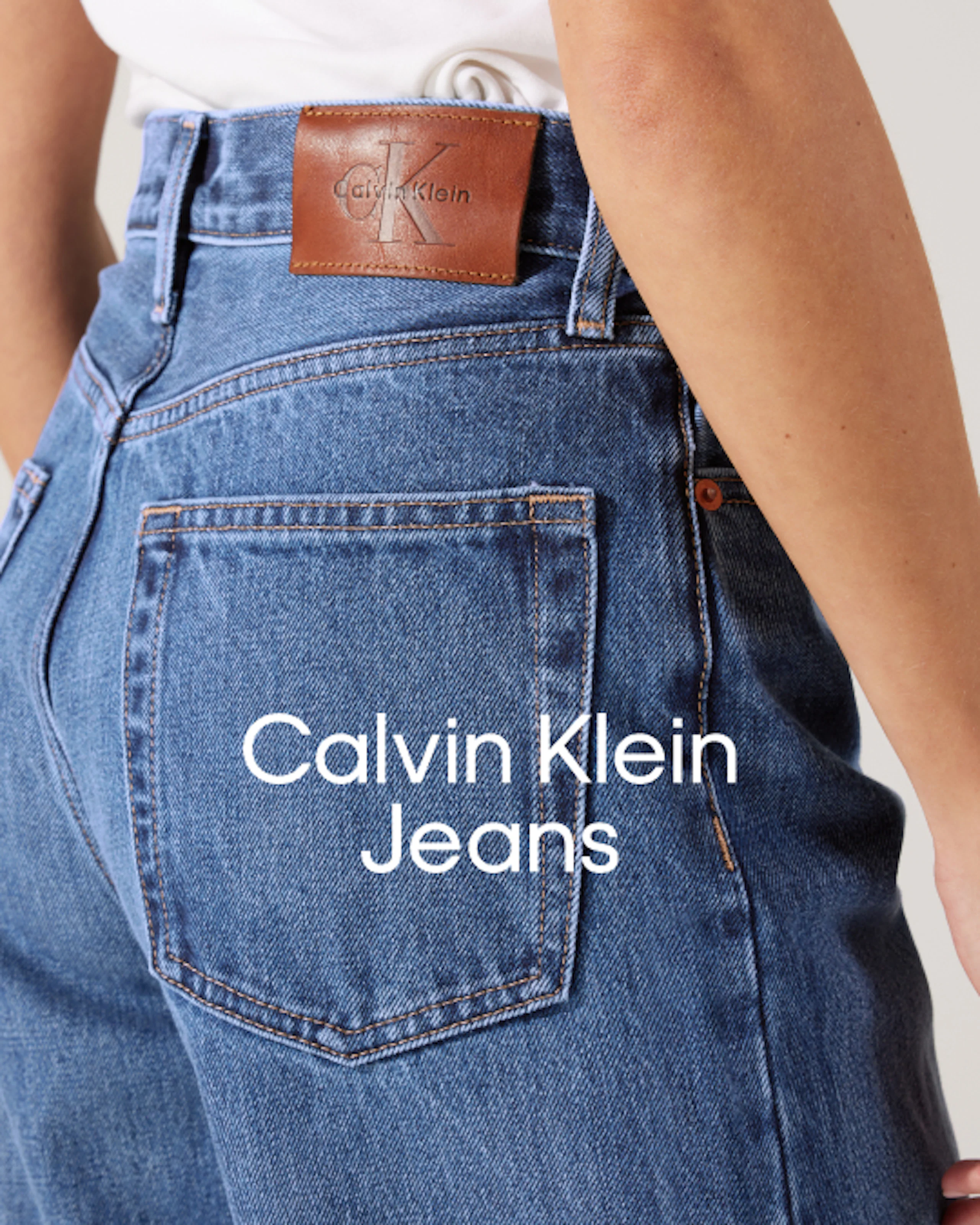 Närbild på Calvin Klein Jeans blå denim med brun läderlogoggapp på midjeband, som visar detalj av bakficka.
