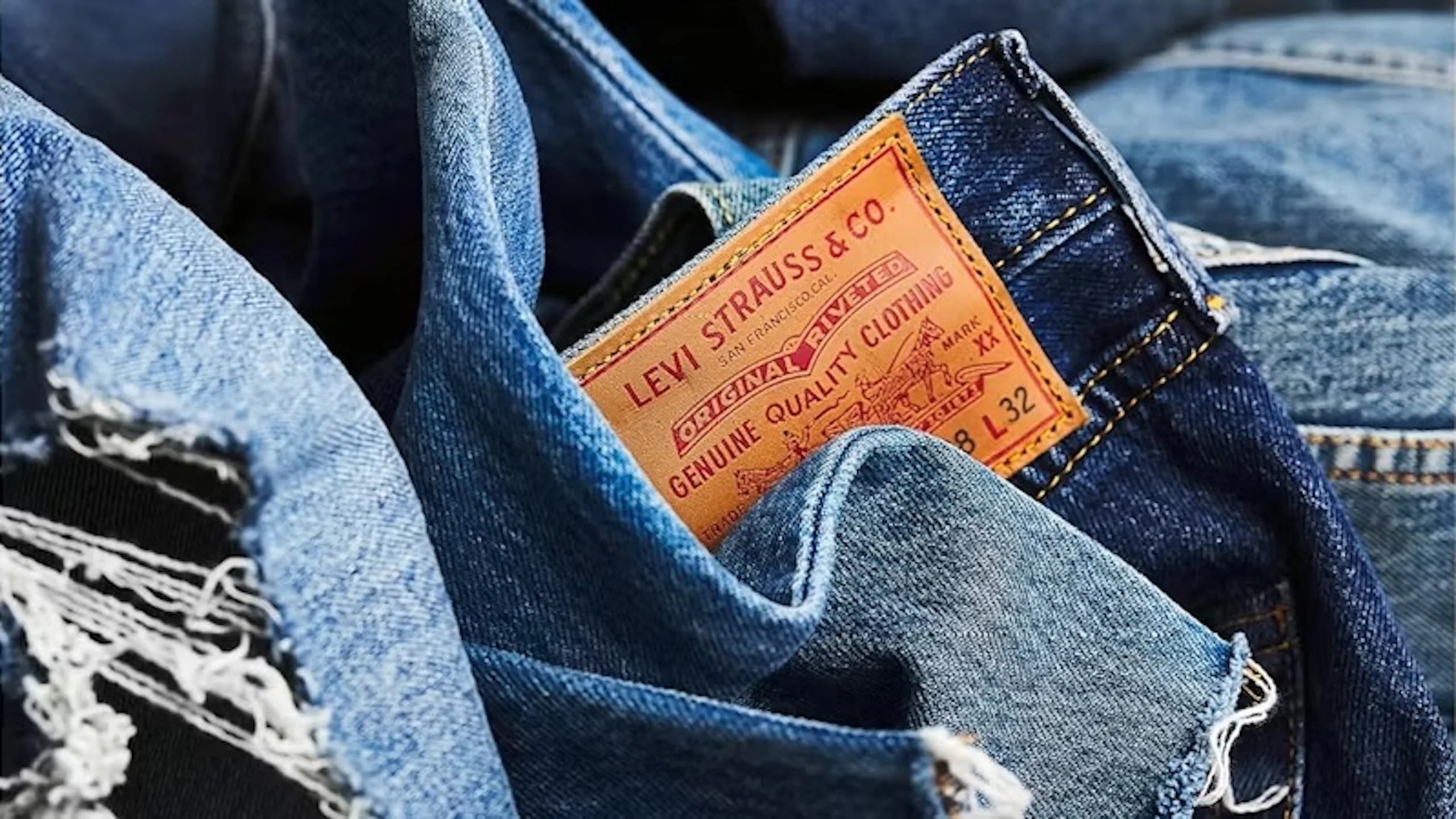 Lähikuva taitetuista sinisistä farkuista, joissa näkyy ruskea Levi Strauss & Co. -nahkalappu, ommel ja kulunut kangas.