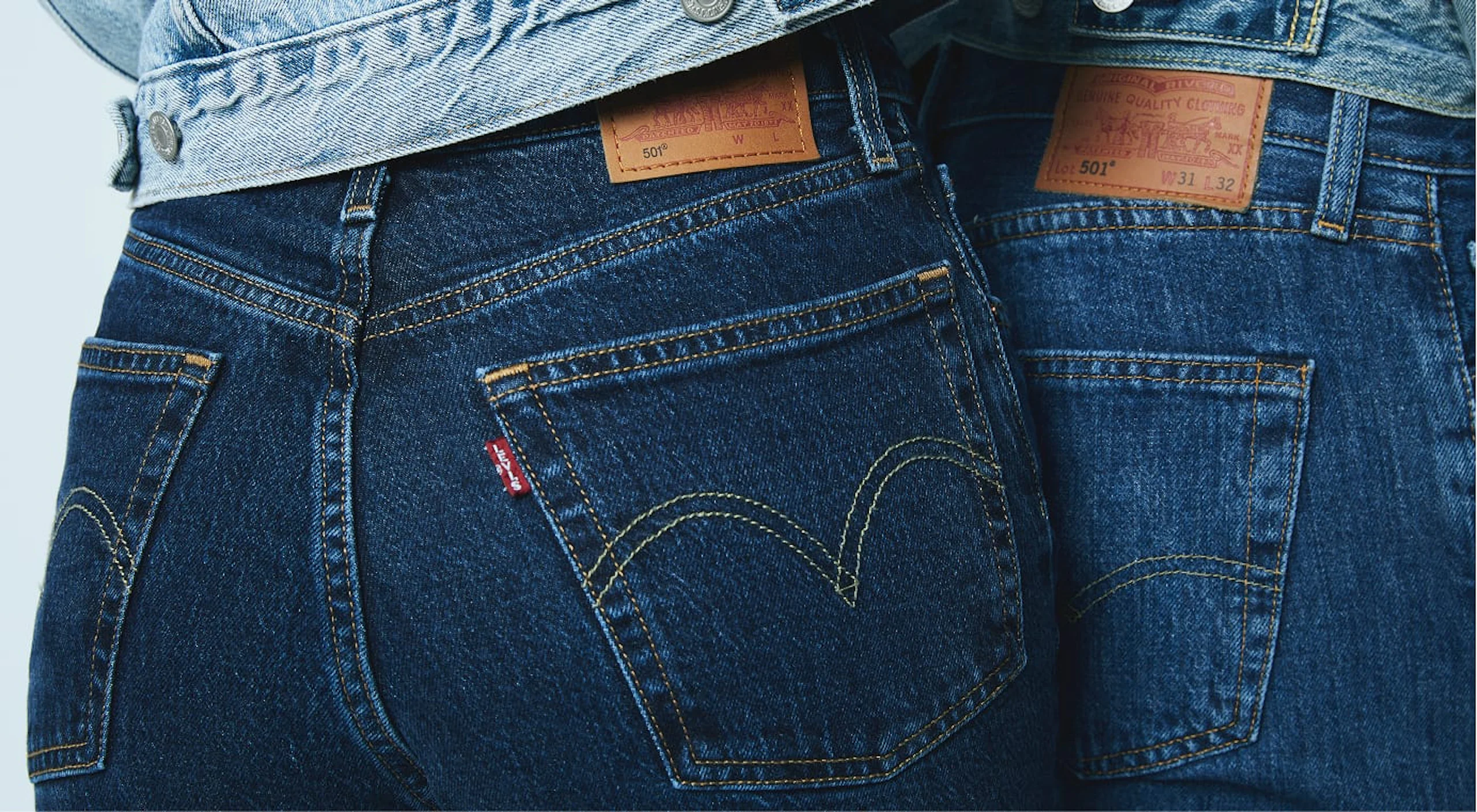 Nærbilde av to personer iført mørkeblå Levi's-jeans, med baklommer, gule sømmer, rød Levi's-flik og lærmerker med merkevaren.